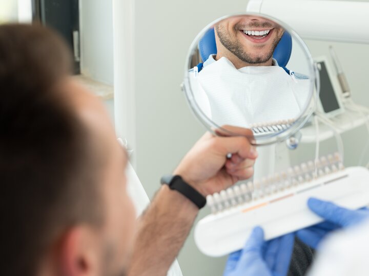 Patient betrachtet seine weißen Zähne nach dem Bleaching im Spiegel